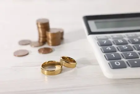 Alimony. Wedding rings, calculator and coins on wooden table, closeup